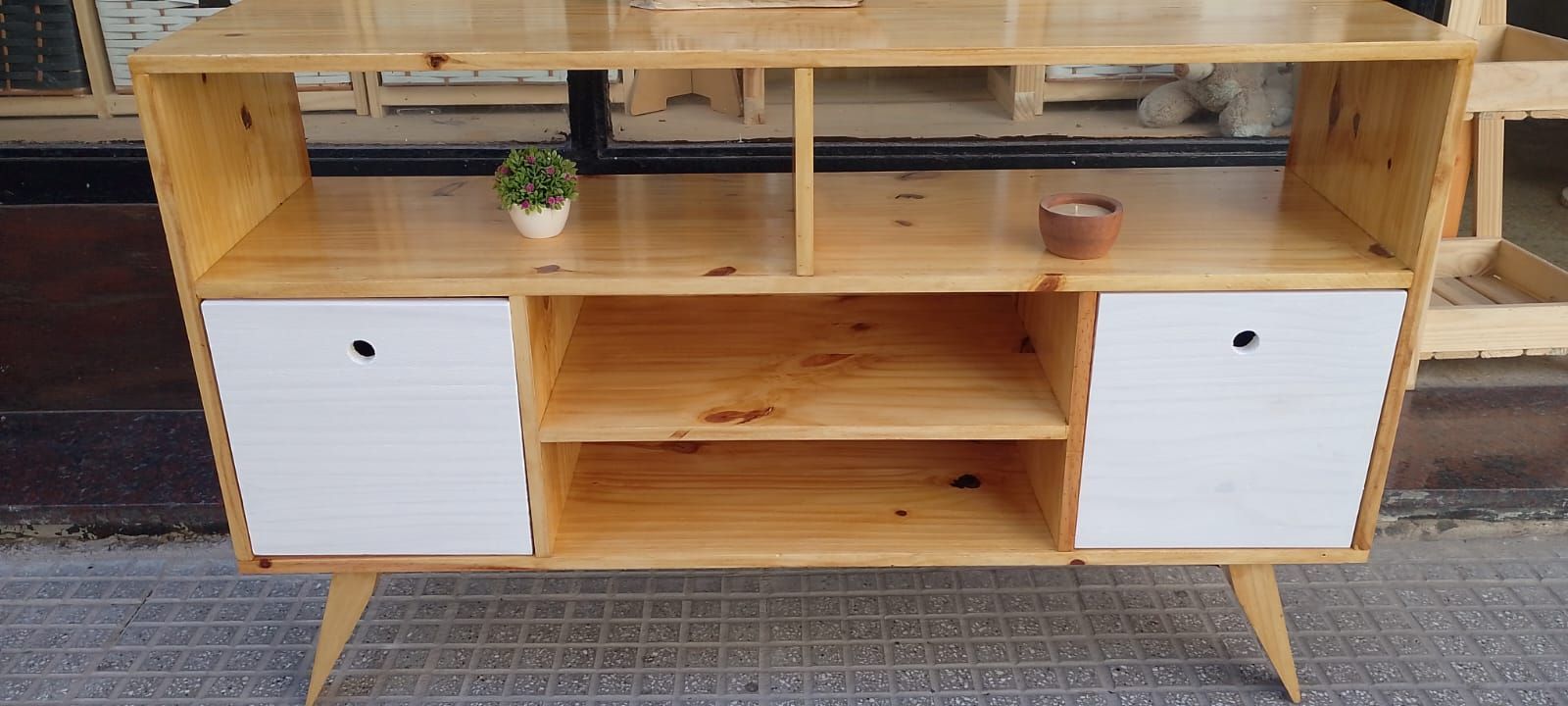 Mueble de madera con dos puertas blancas, estantes, pequeña planta y cuenco.