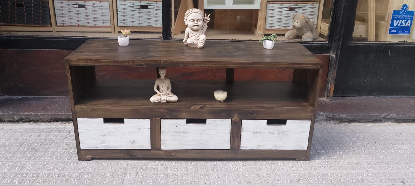 Un armario de madera con tres cajones blancos y estantes abiertos, decorado con estatuas y plantas.
