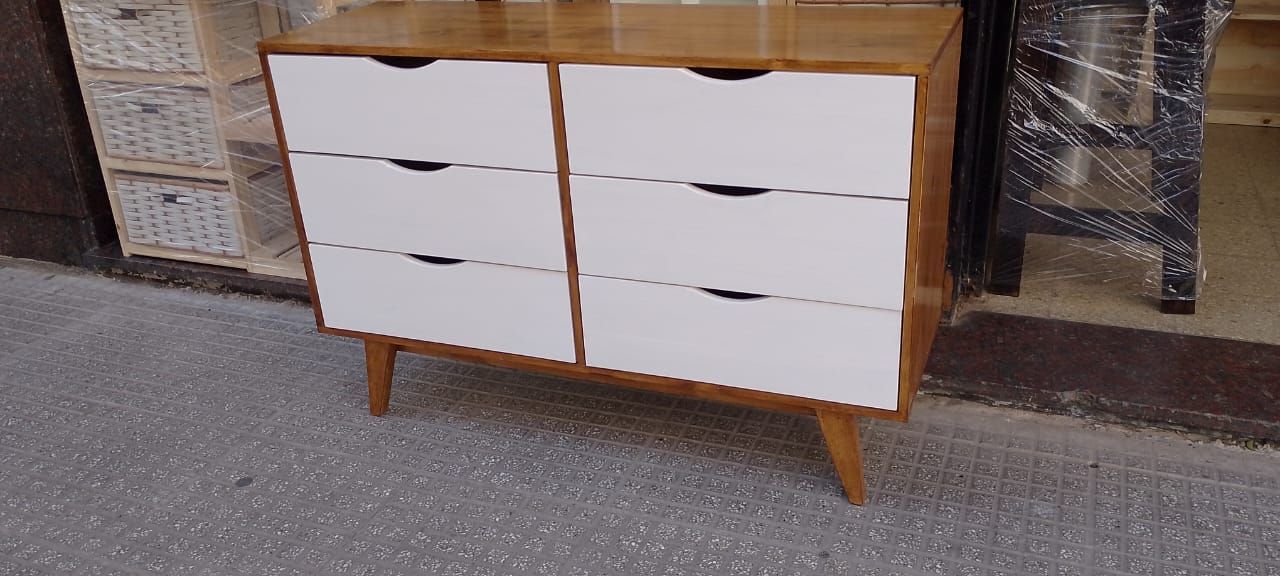 Una cómoda de madera con cajones blancos, colocada sobre una superficie gris al aire libre.
