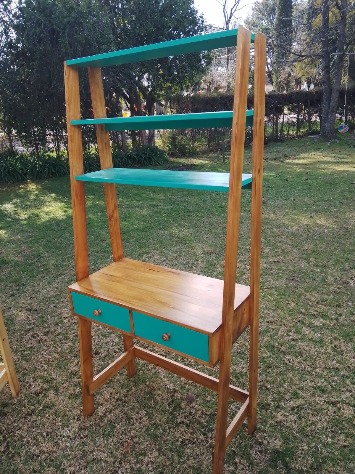 Escritorio de madera con estantes y cajones de color verde azulado en un entorno al aire libre.