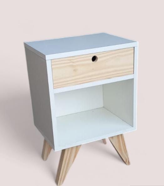 Mesita de noche de madera y color blanco con cajón y estante, patas en ángulo, sobre fondo rosa.