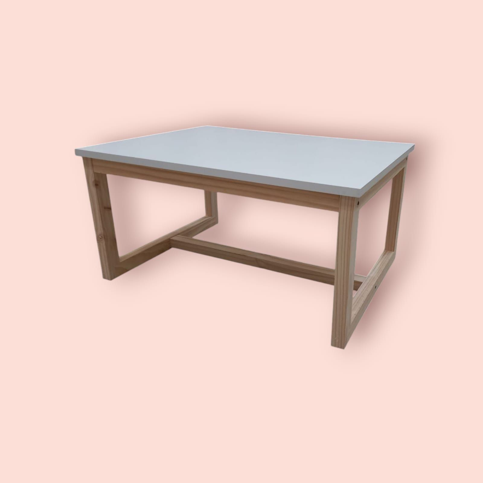 Una mesa rectangular de madera con tapa blanca y marco marrón claro, sobre un fondo color melocotón.