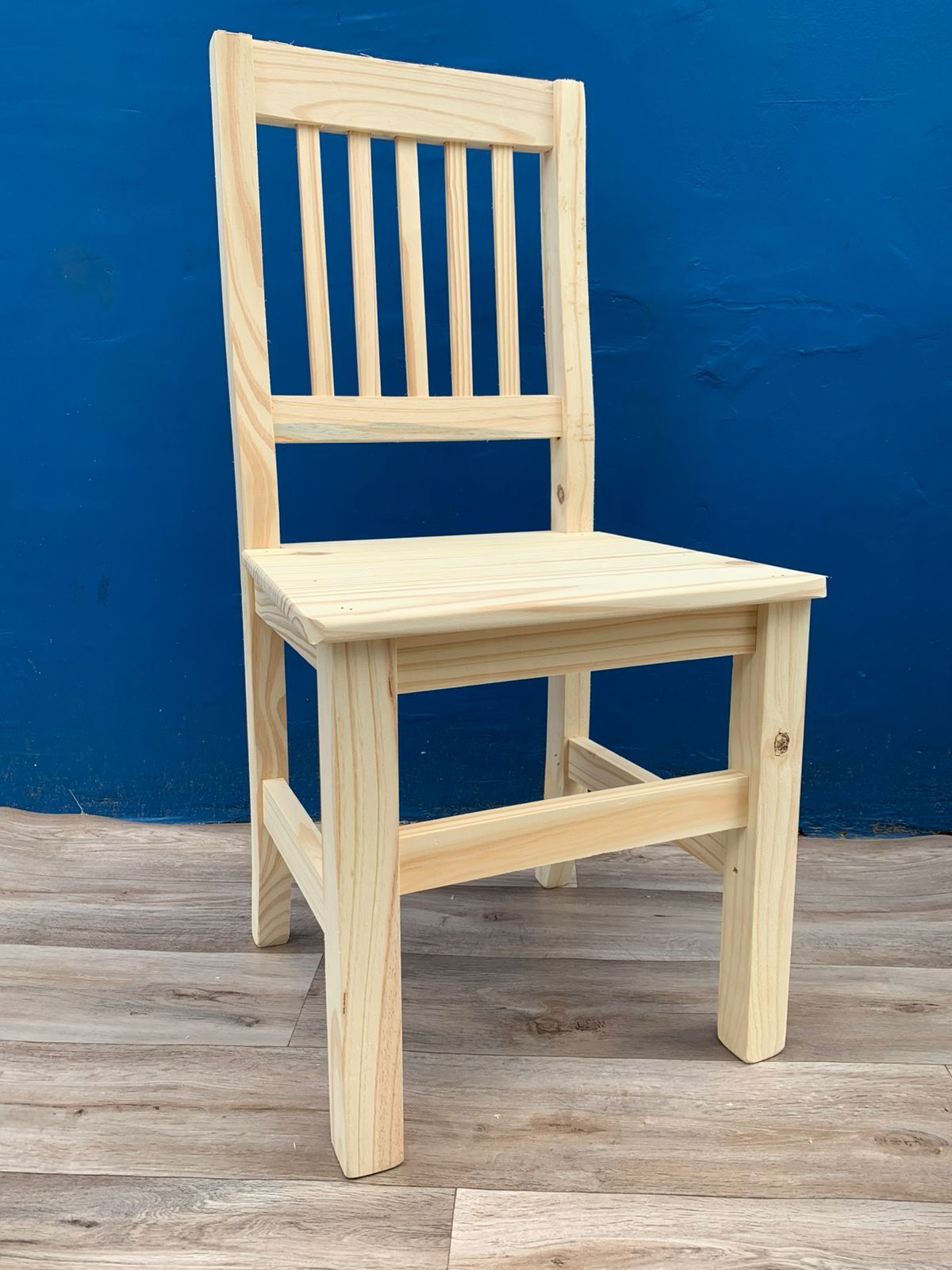 Silla de madera con respaldo de listones contra una pared azul.