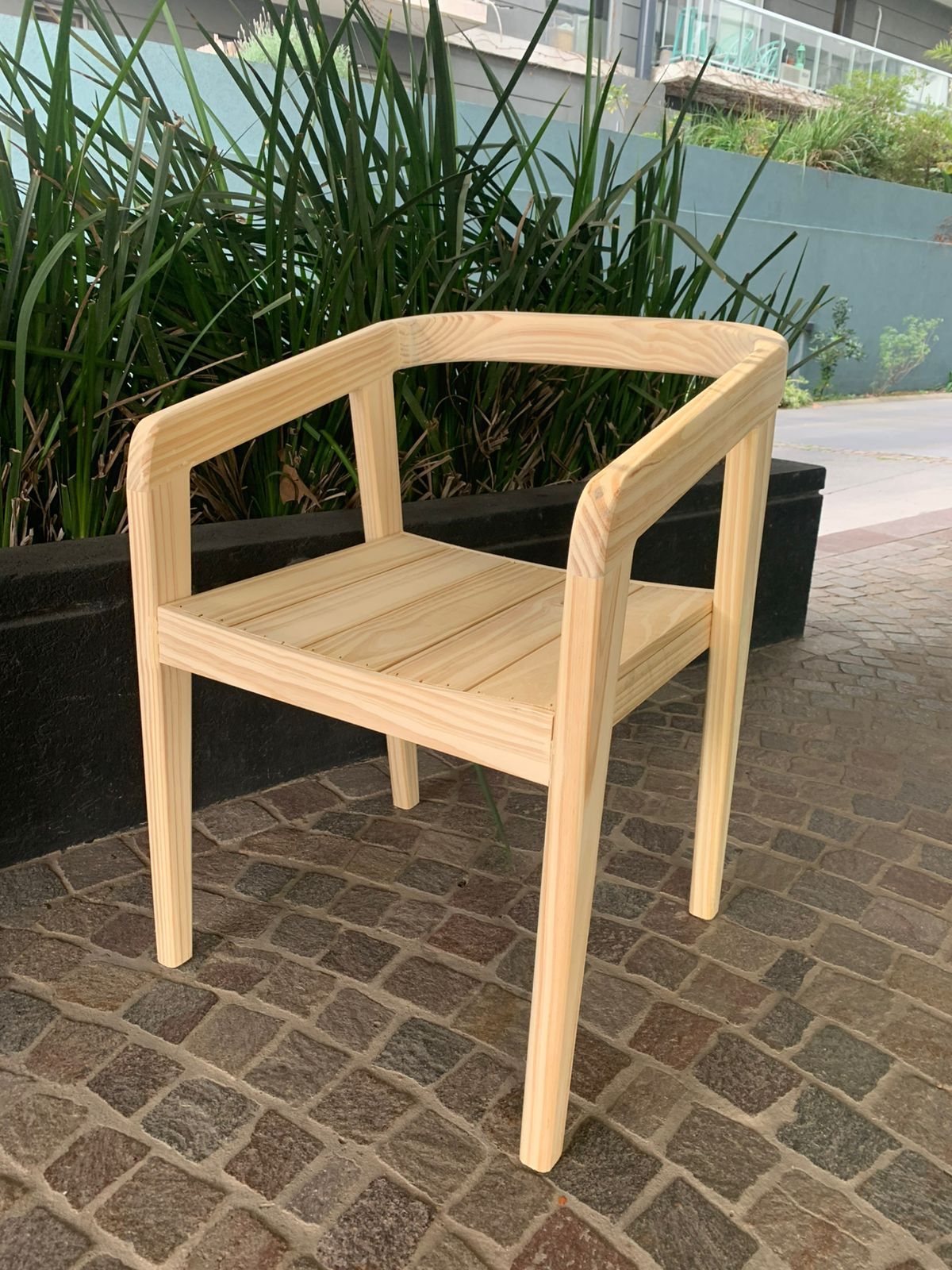 Silla de madera sobre una superficie de ladrillo, con vegetación al fondo.