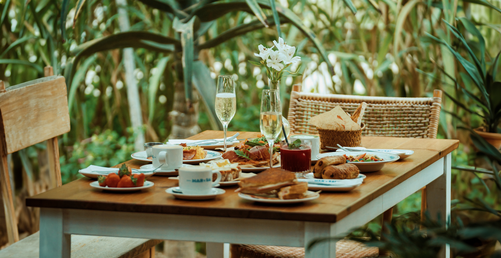 A table topped with plates of food and drinks in a garden.