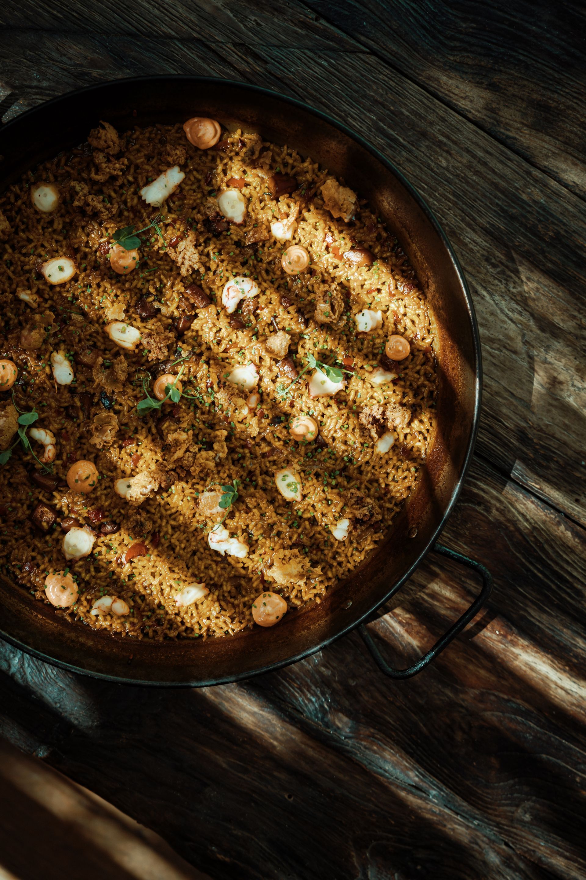 A pan filled with rice and shrimp is sitting on a wooden table.