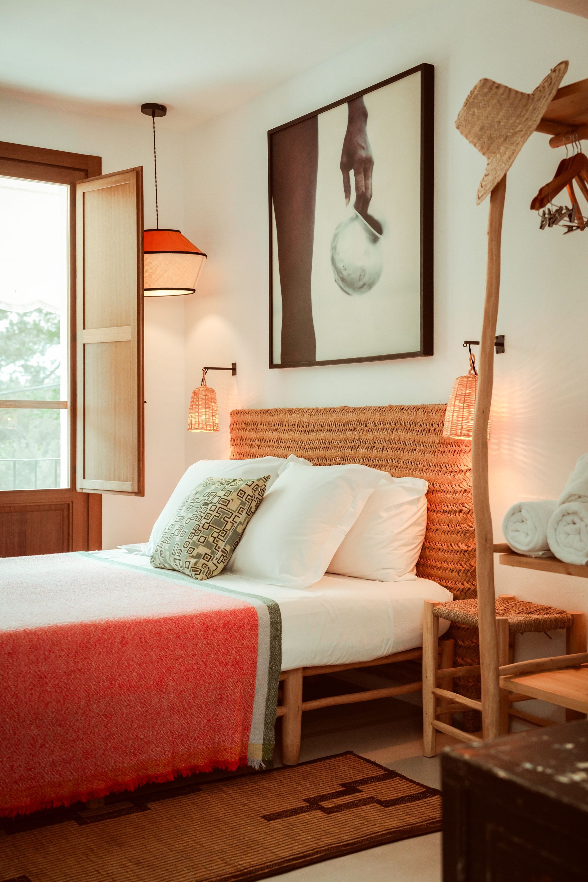 A bedroom with a bed , a straw hat and a painting on the wall.