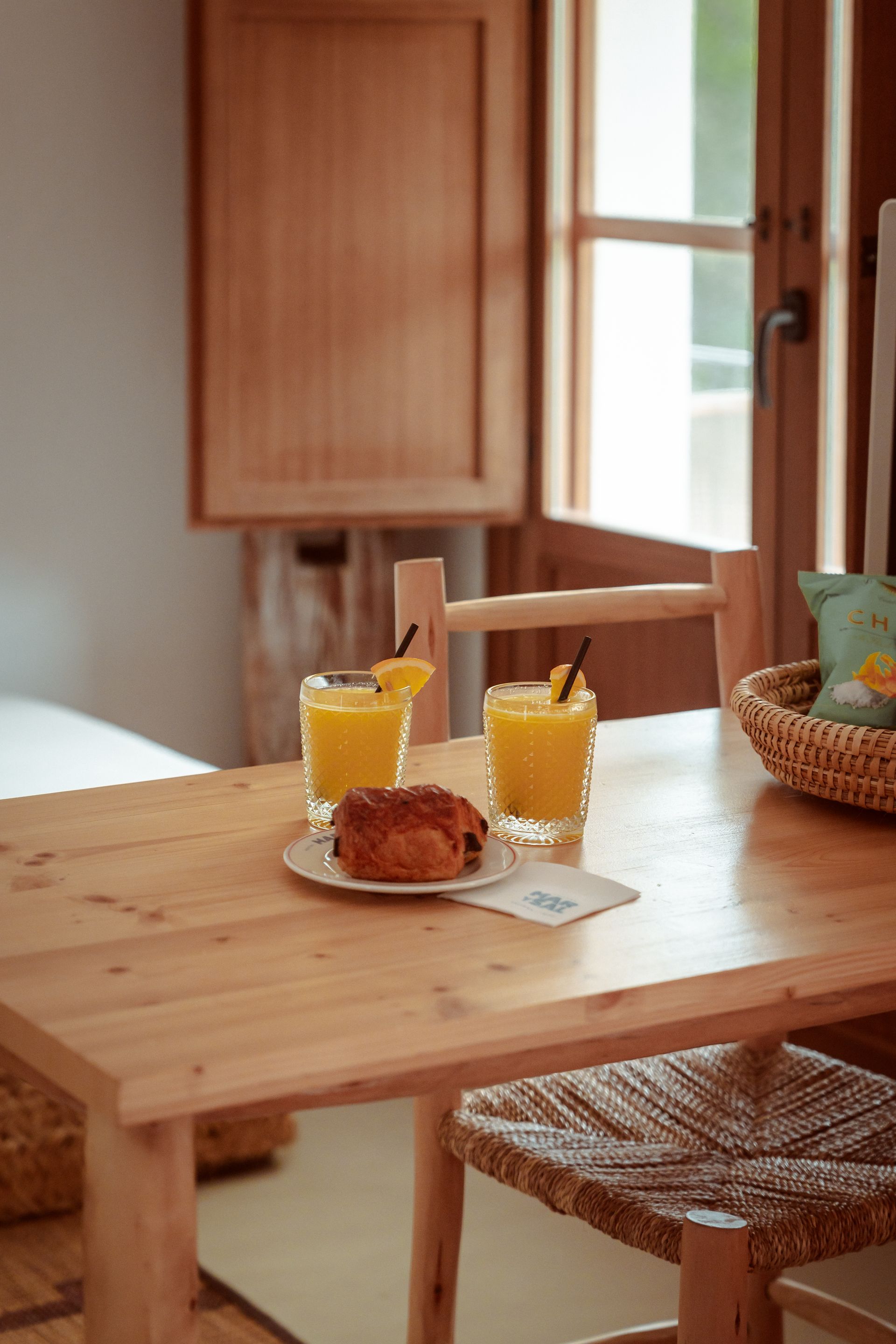 A wooden table with two glasses of orange juice and a croissant on it.