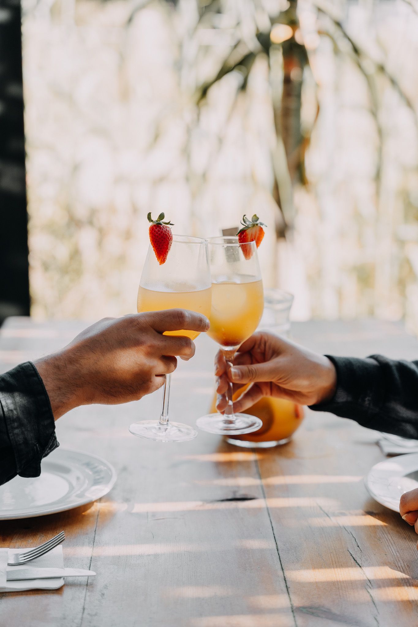 Dos personas brindando con vasos de líquido naranja adornado con fresas sobre una mesa de madera.