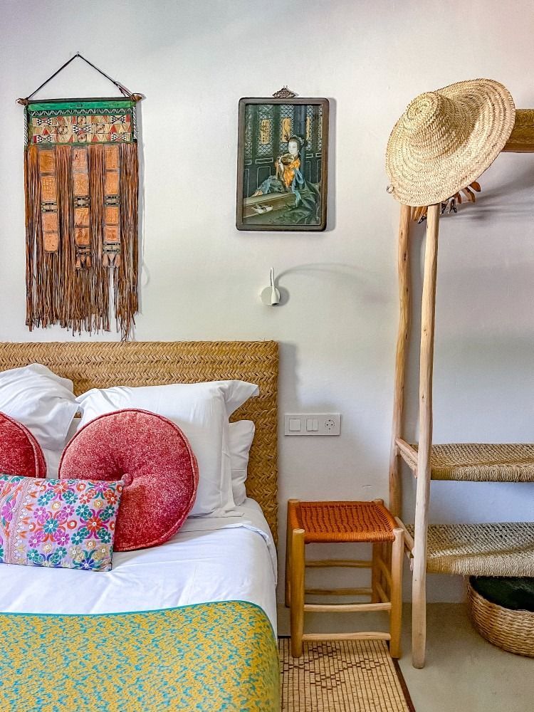 A bedroom with a bed , a stool , a hat and a painting on the wall.