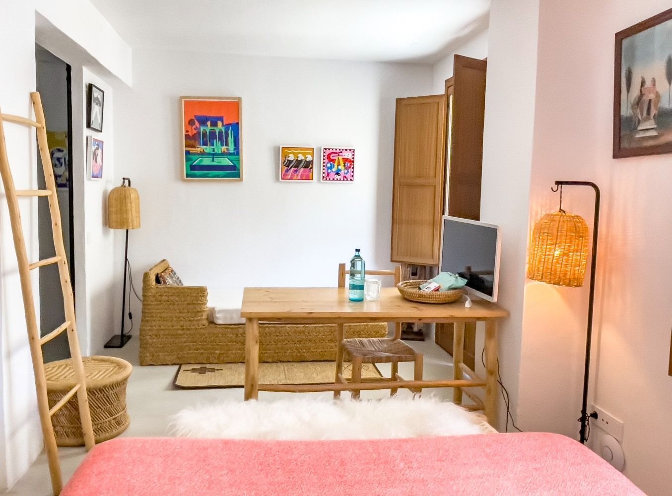 A bedroom with a bed , desk , couch and paintings on the wall.