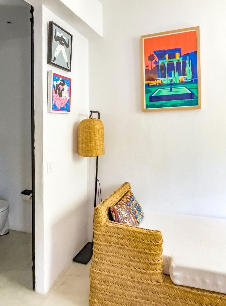 A bedroom with a bed , chair , lamp and paintings on the wall.