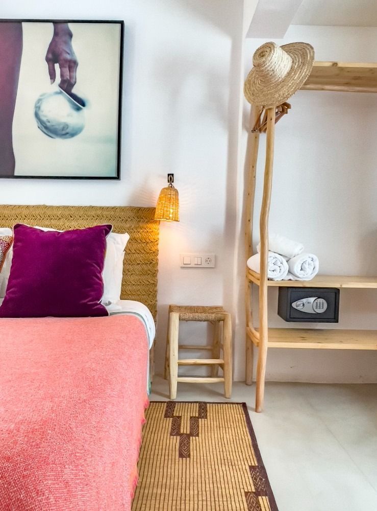 A bedroom with a bed , a stool , a picture on the wall and a hat hanging on a rack.