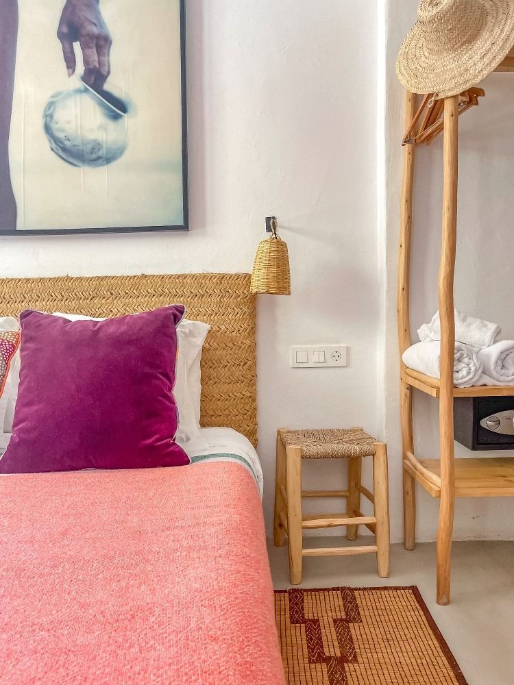 A bedroom with a bed , nightstand , stool and a painting on the wall.