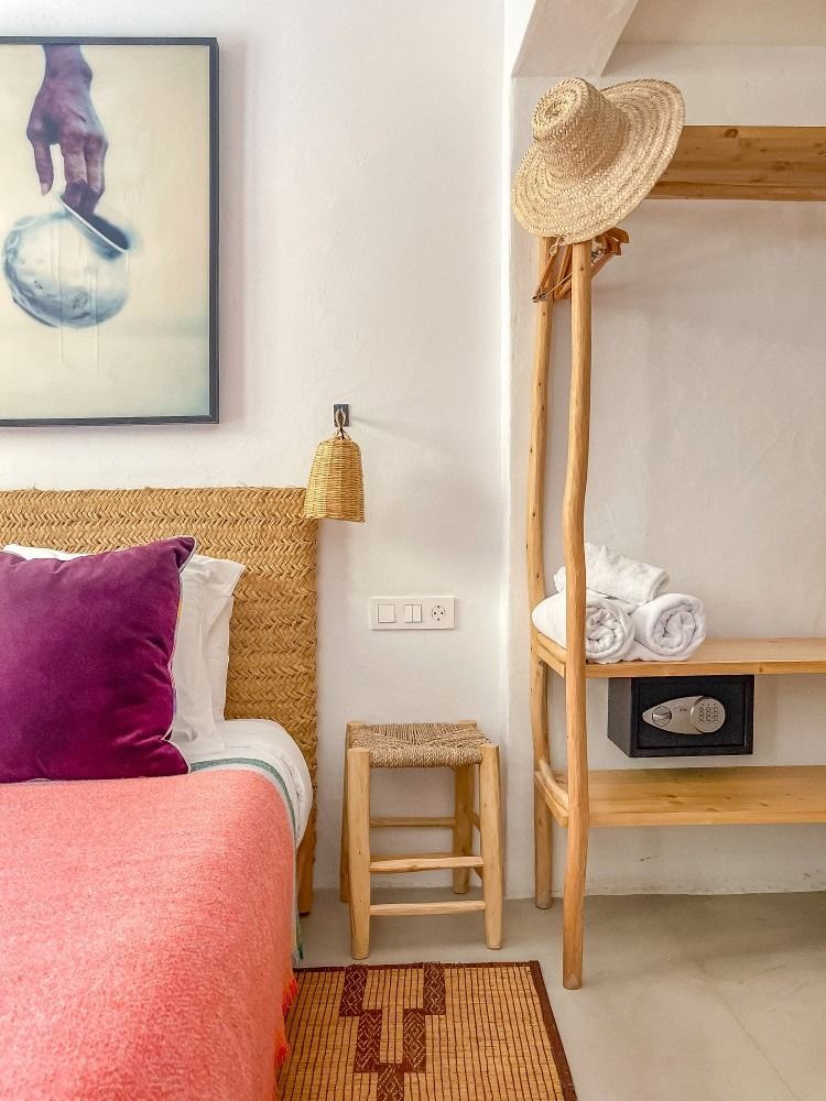 A bedroom with a bed , stool , hat and a picture on the wall.