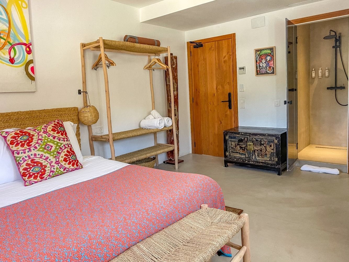 A bedroom with a bed , bench , dresser and shower.