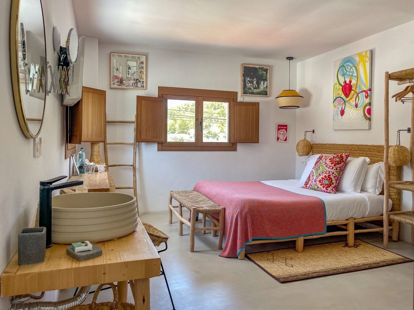 A bedroom with a bed , sink , mirror and window.