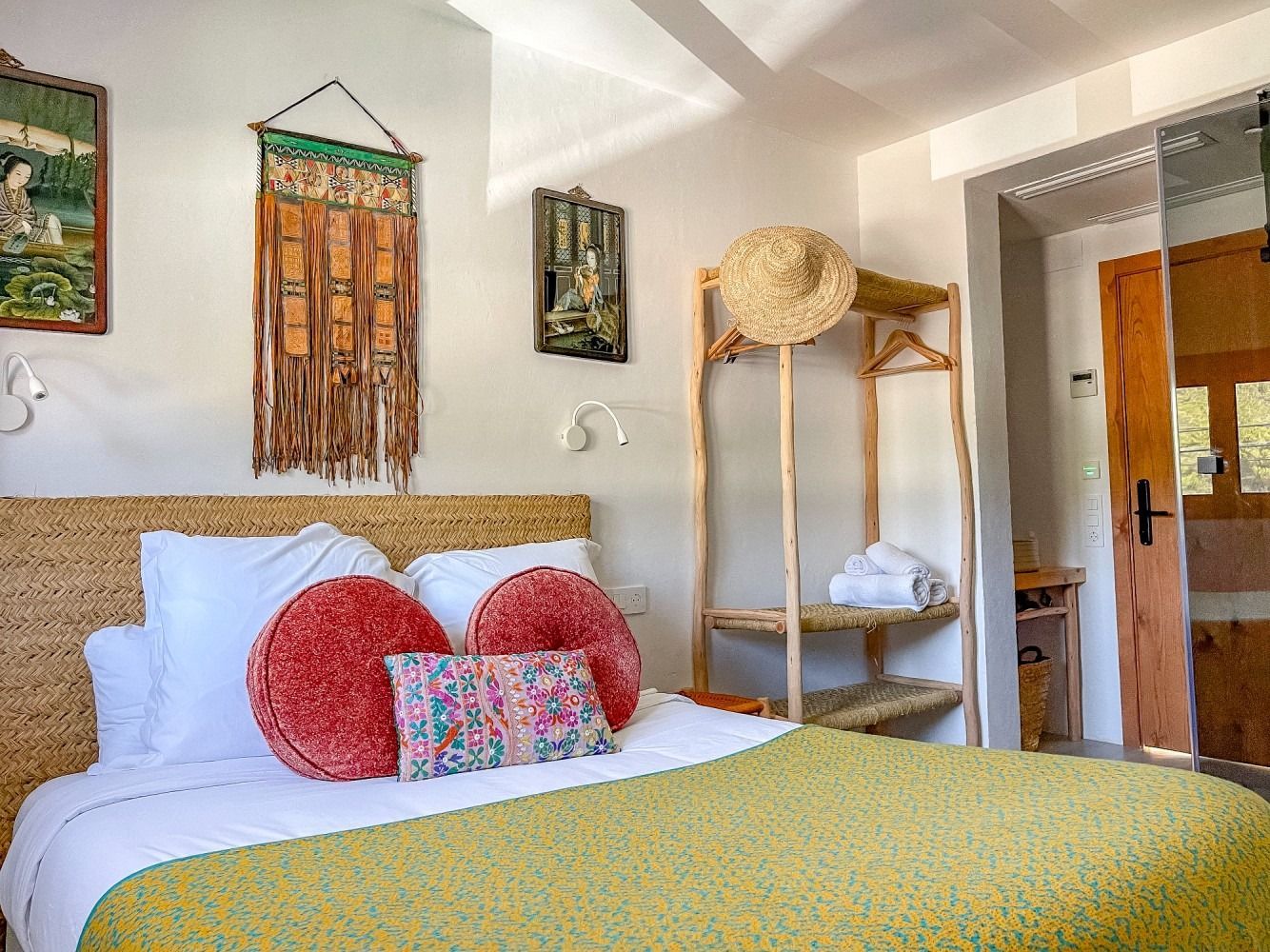 A bedroom with a bed , a wicker headboard , and a straw hat hanging on the wall.