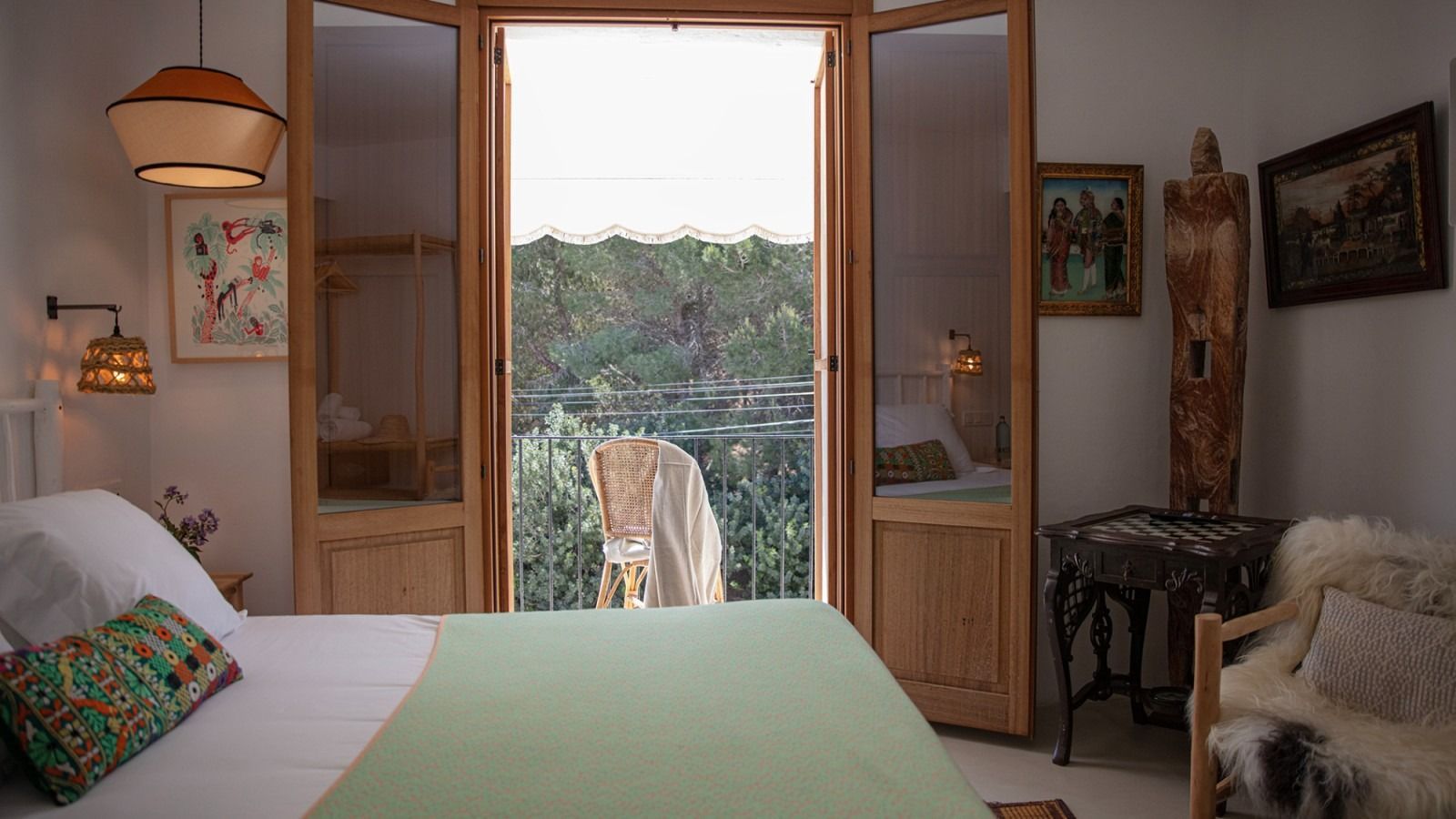 A bedroom with a bed and a balcony with a view of trees.