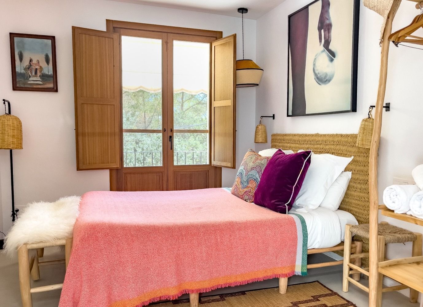 There is a bed with a pink blanket and purple pillows in the room.