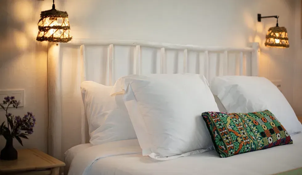 A bed with white sheets and pillows in a bedroom with two lamps on the wall.