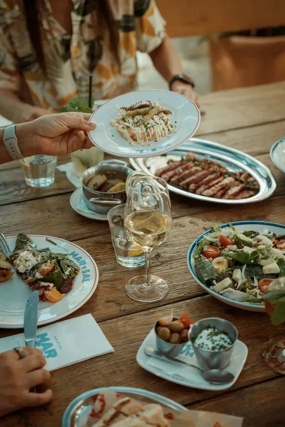A group of people are sitting at a table eating food and drinking wine.
