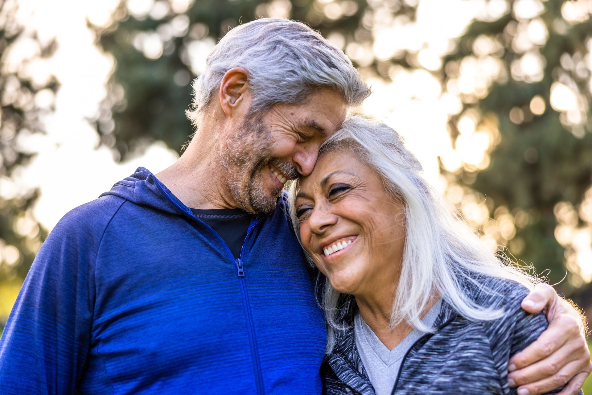 An elderly couple is walking down a sidewalk in a park.