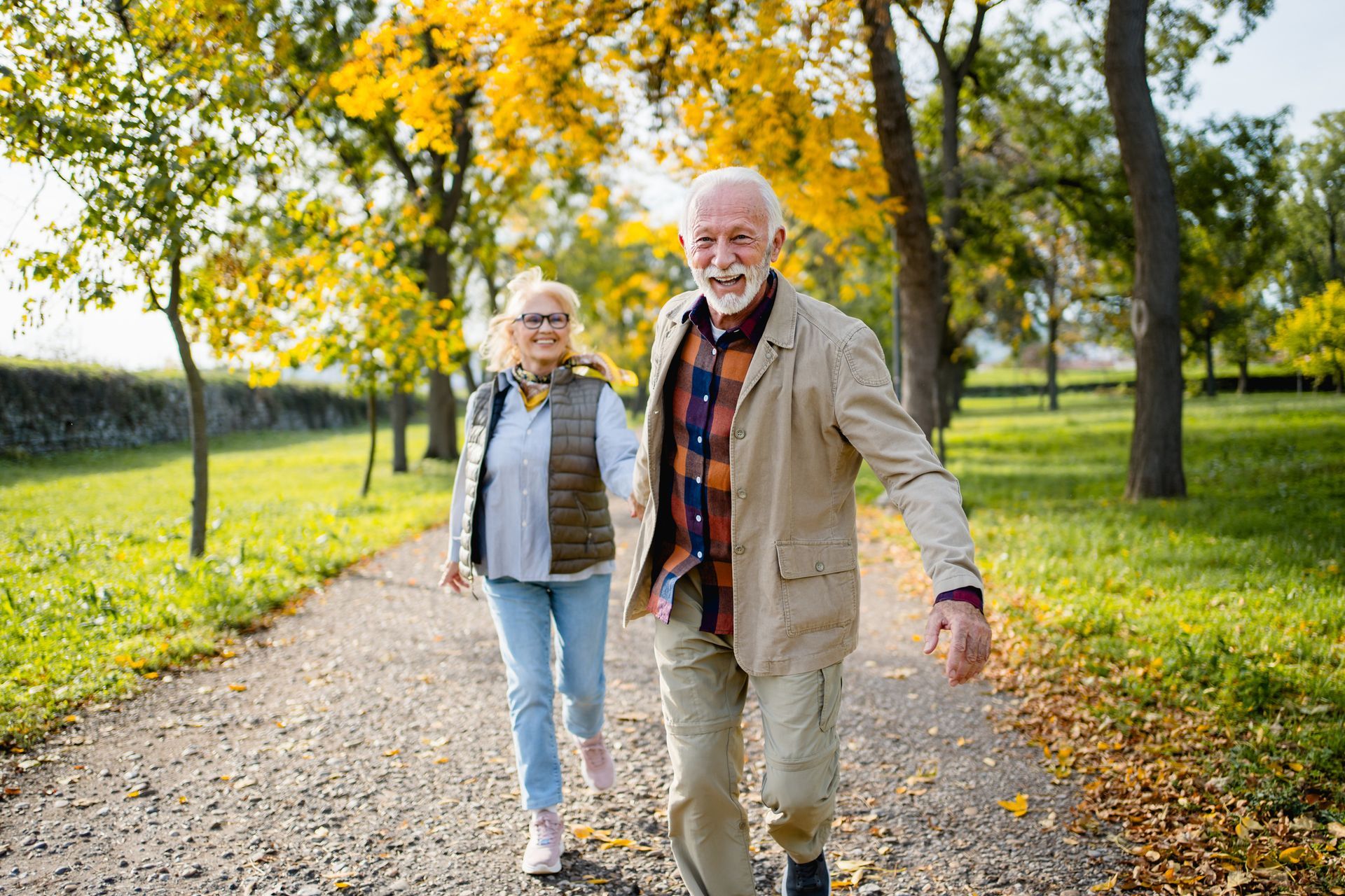 An elderly couple is walking down a path in a park.