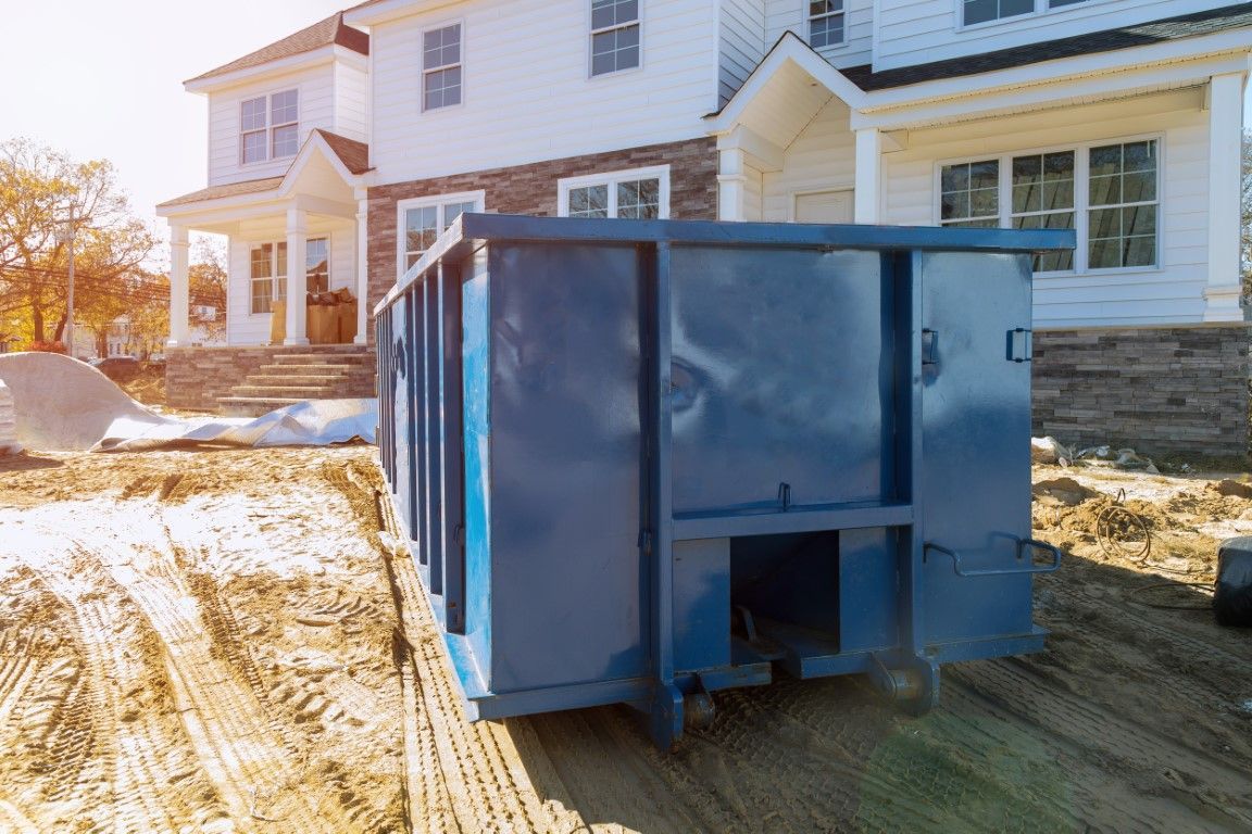 Blue construction dumpster on a snowy driveway beside a white house under construction