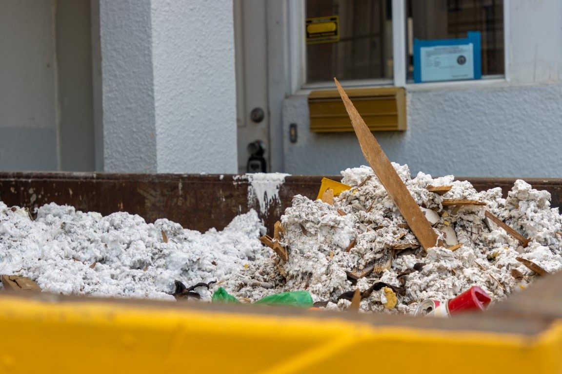 Snow piled behind a yellow barrier outside a building, with a wooden plank sticking out.