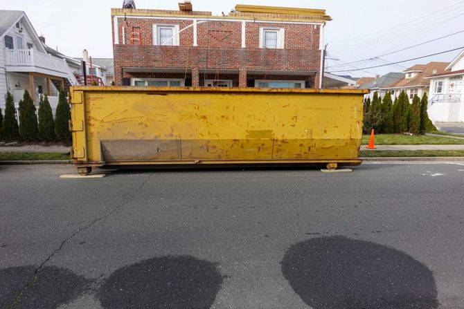 Large yellow dumpster on a residential street in front of a brick house