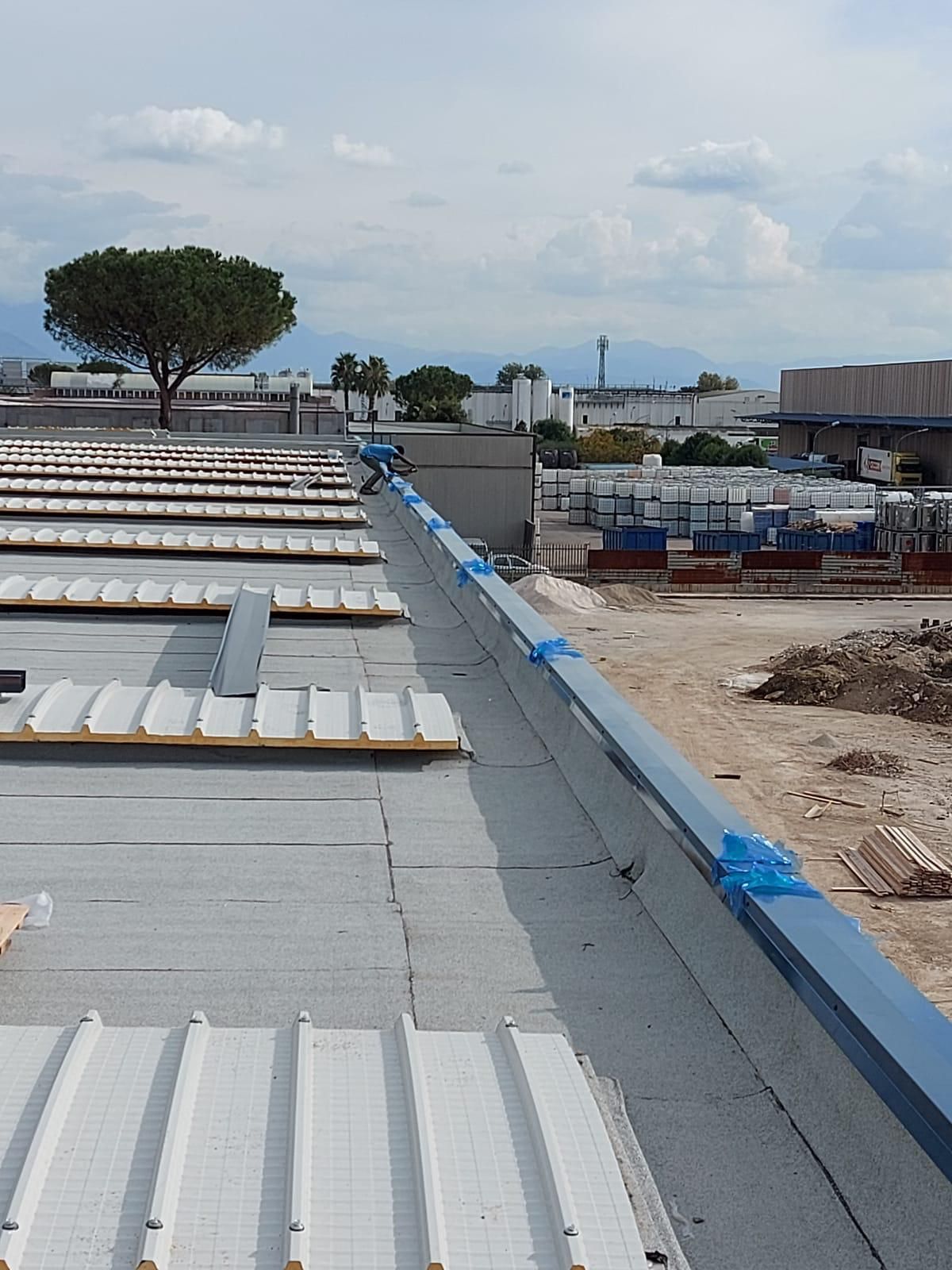 Cantiere edile sul tetto con pannelli grigi, materiali bianchi e ringhiere blu sotto un cielo nuvoloso.