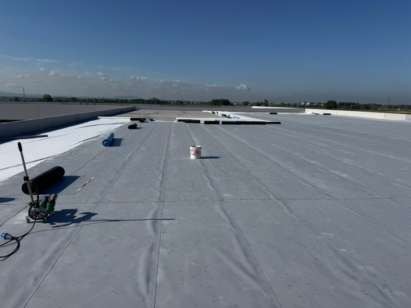 Tetto bianco piatto con unità di climatizzazione e un cielo azzurro limpido in lontananza.