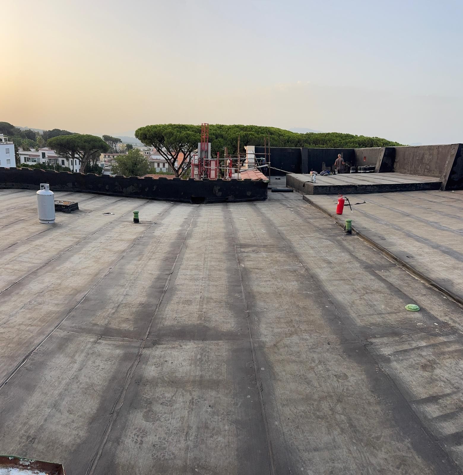 Terrazza in cemento sul tetto con attrezzature industriali e uno skyline in lontananza al tramonto.