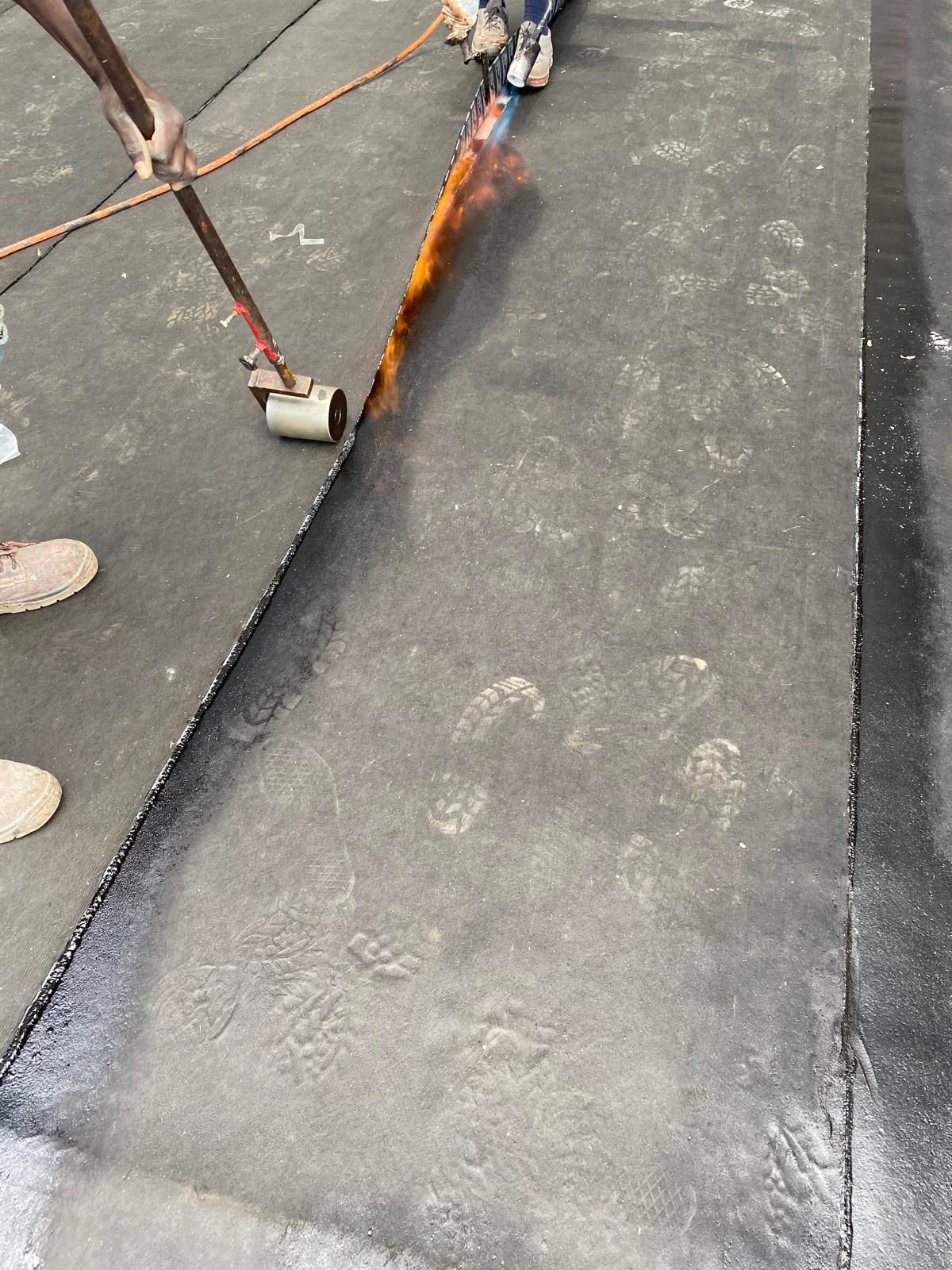 Operai che utilizzano una fiamma ossidrica per sigillare una giuntura su una membrana nera del tetto.