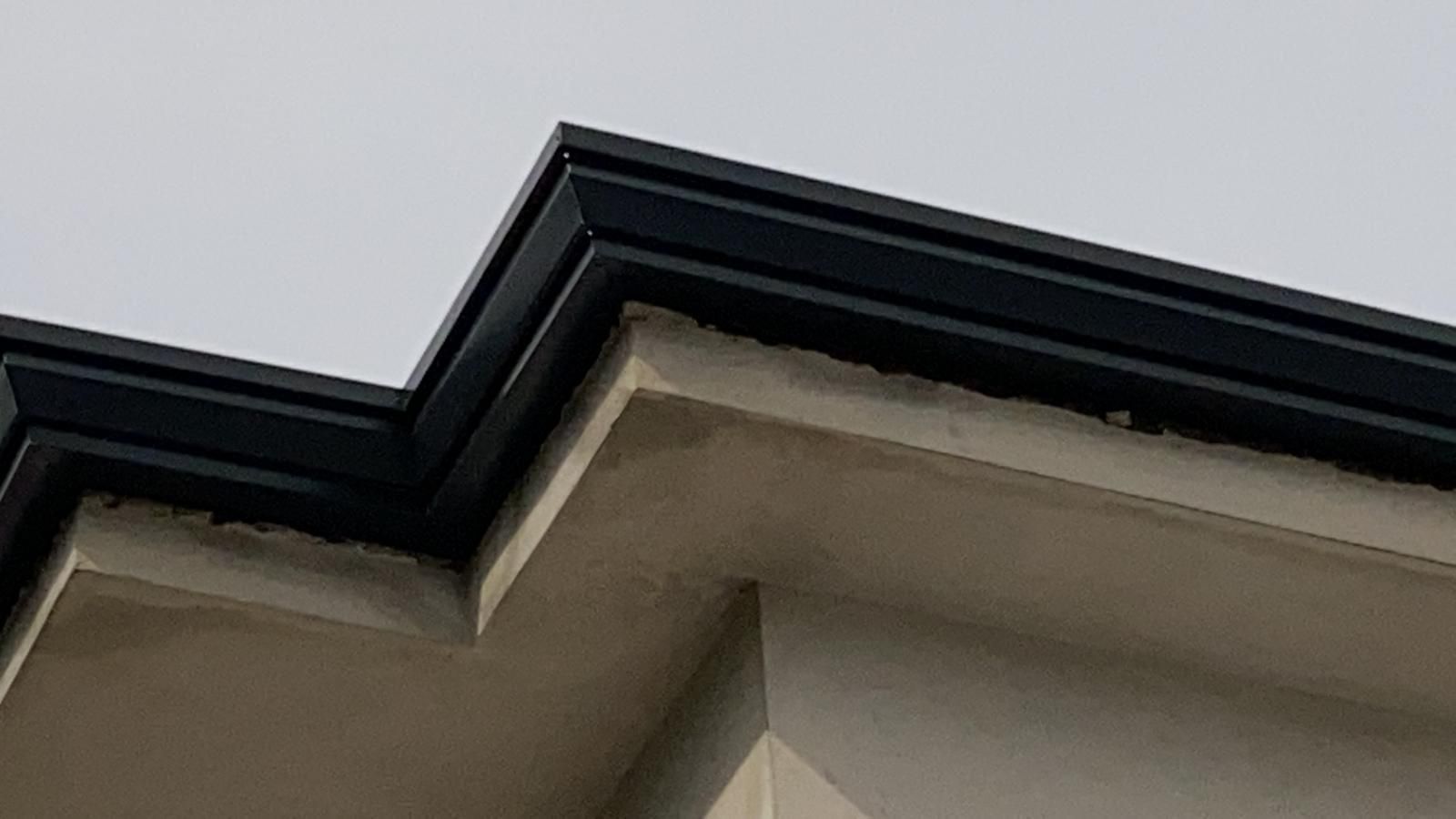 Primo piano della grondaia di una casa con finiture scure sullo sfondo di un cielo grigio.