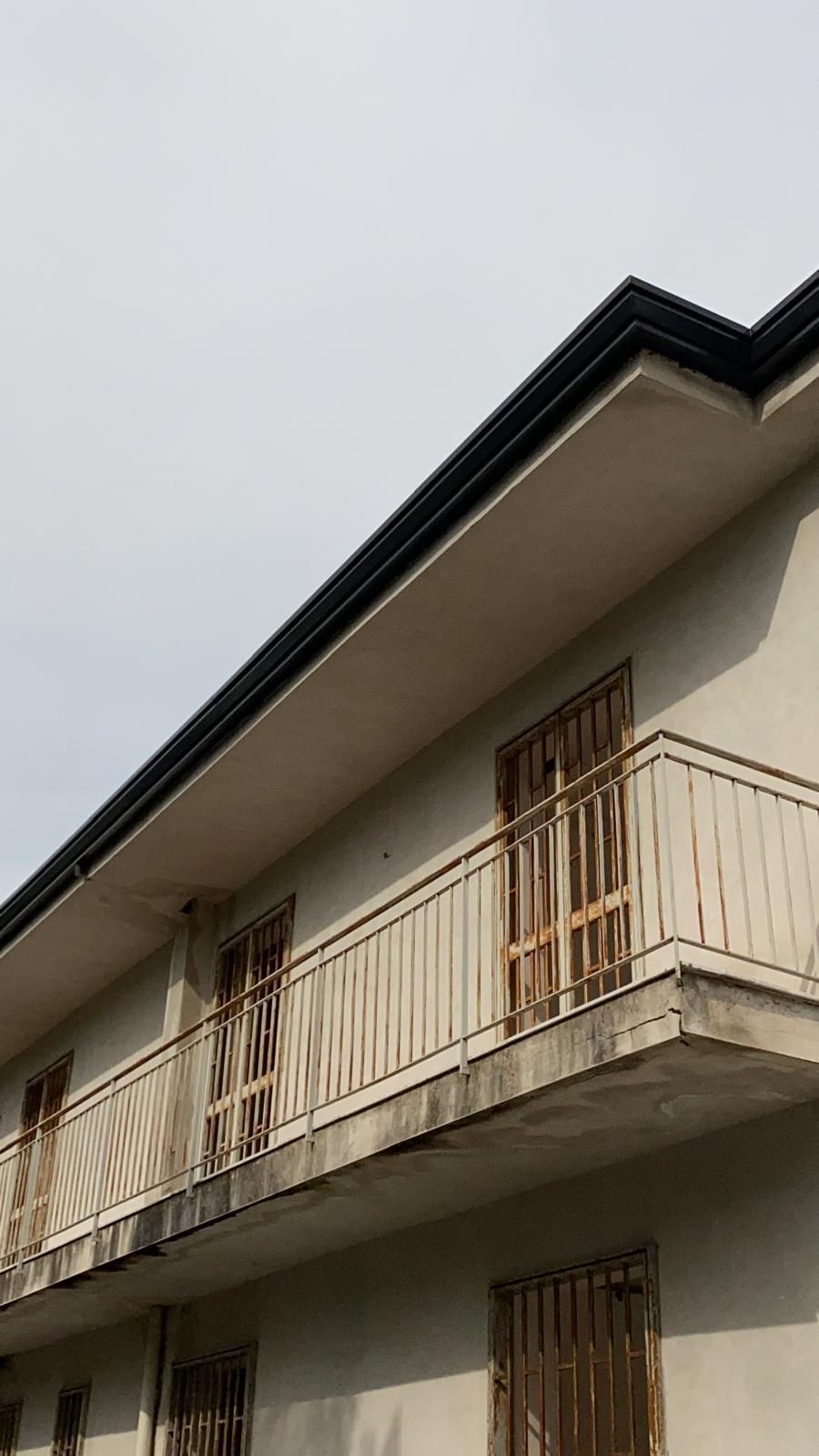 Edificio residenziale beige a due piani con ringhiere metalliche sui balconi e finestre con inferriate, sotto un cielo nuvoloso.