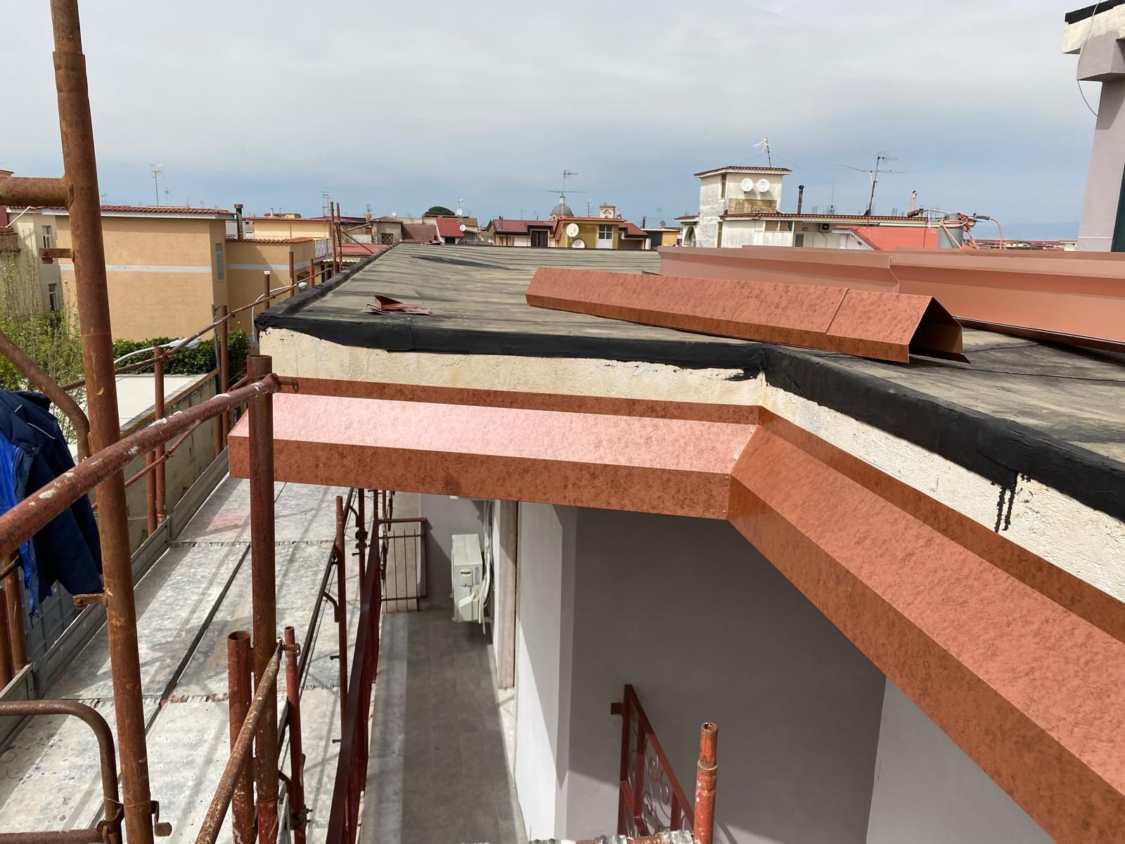 Tetto in costruzione con operai, impalcature e tegole arrotolate sotto un cielo limpido.