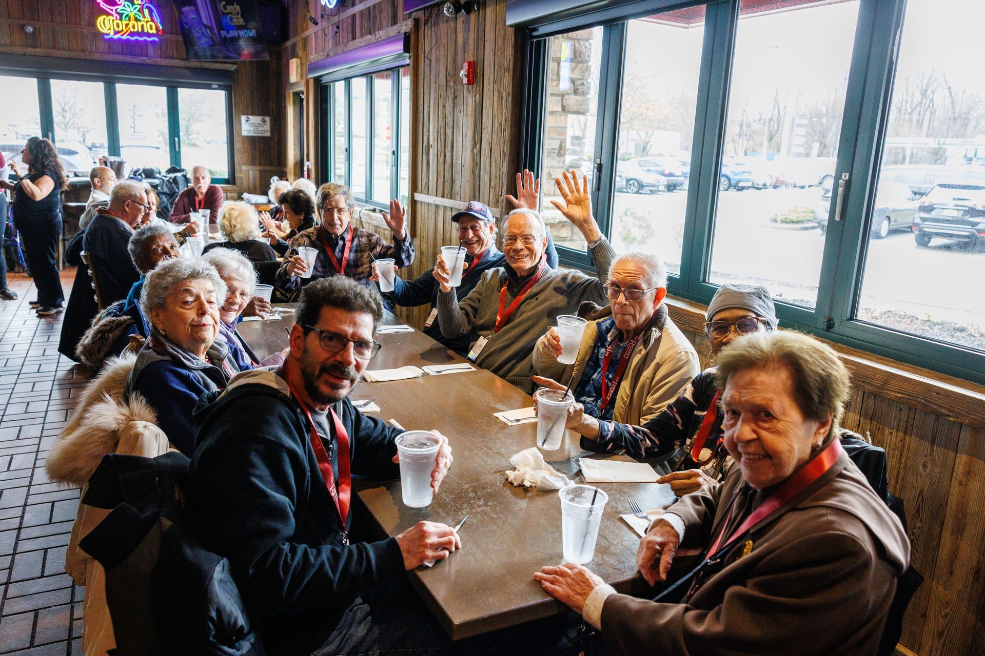 People seated at a restaurant table, drinking from plastic cups by large windows.