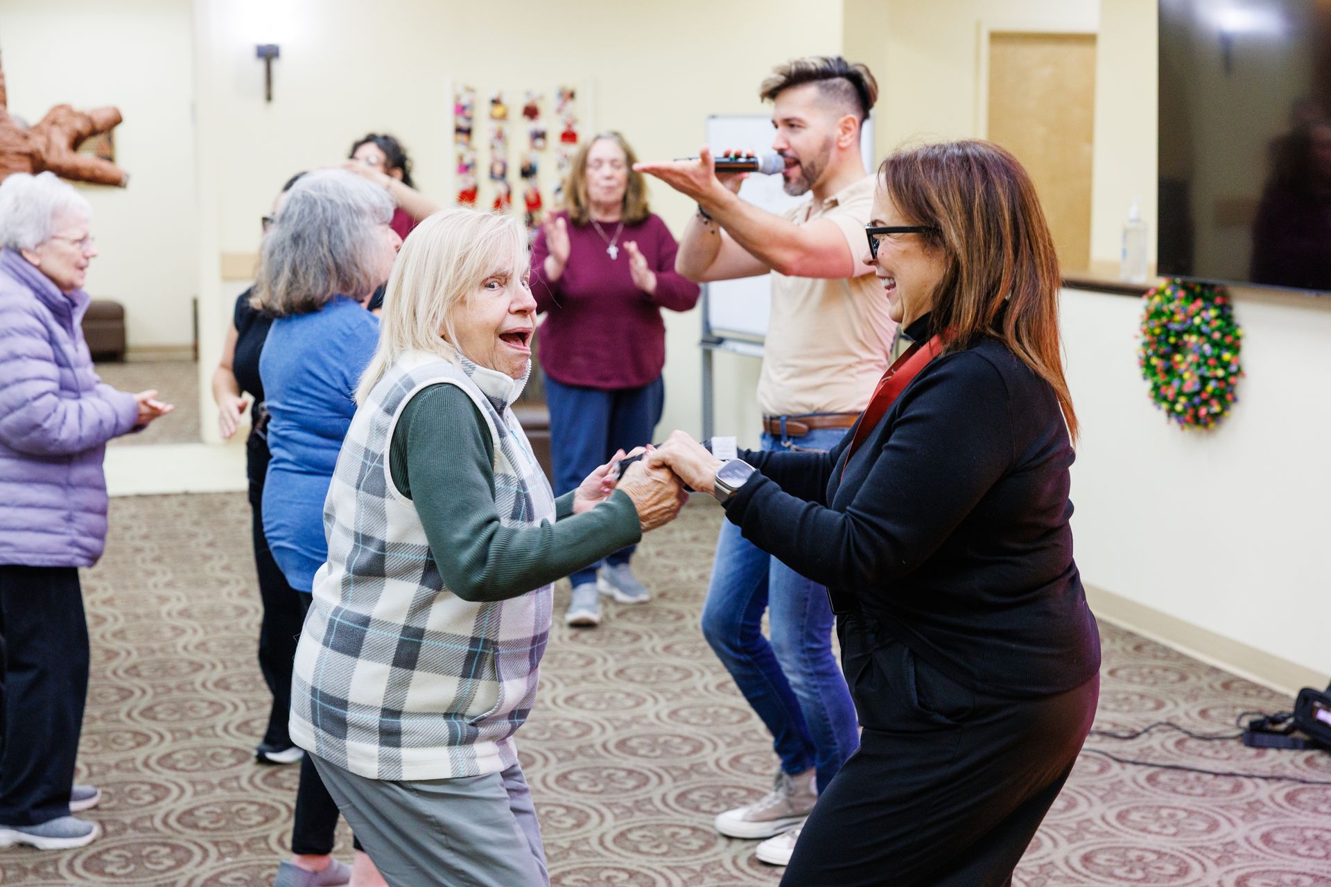 People dancing and smiling in a community hall, holding hands in a festive group activity