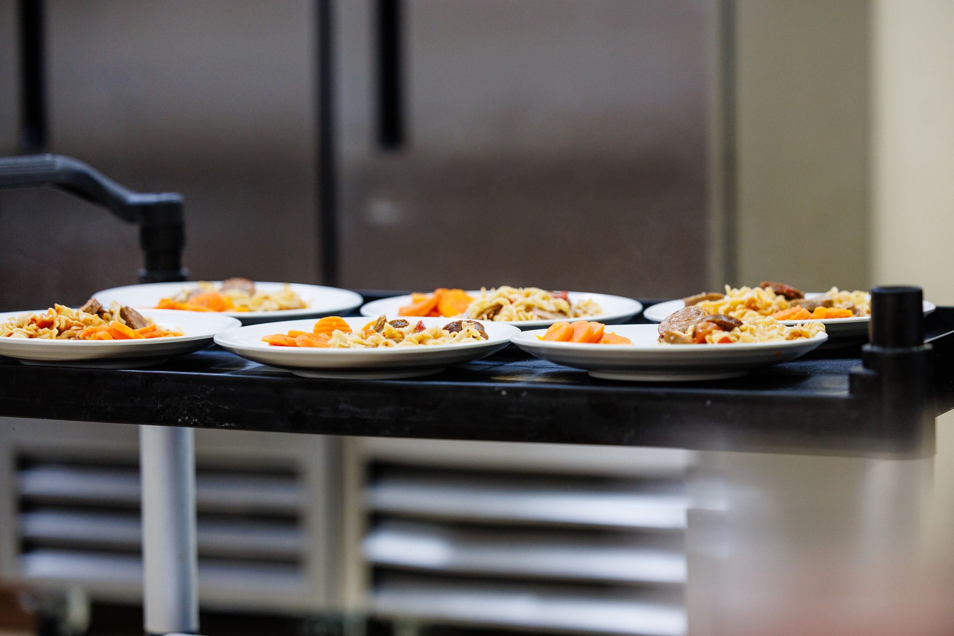 Several white plates of food on a black serving cart in a kitchen or cafeteria