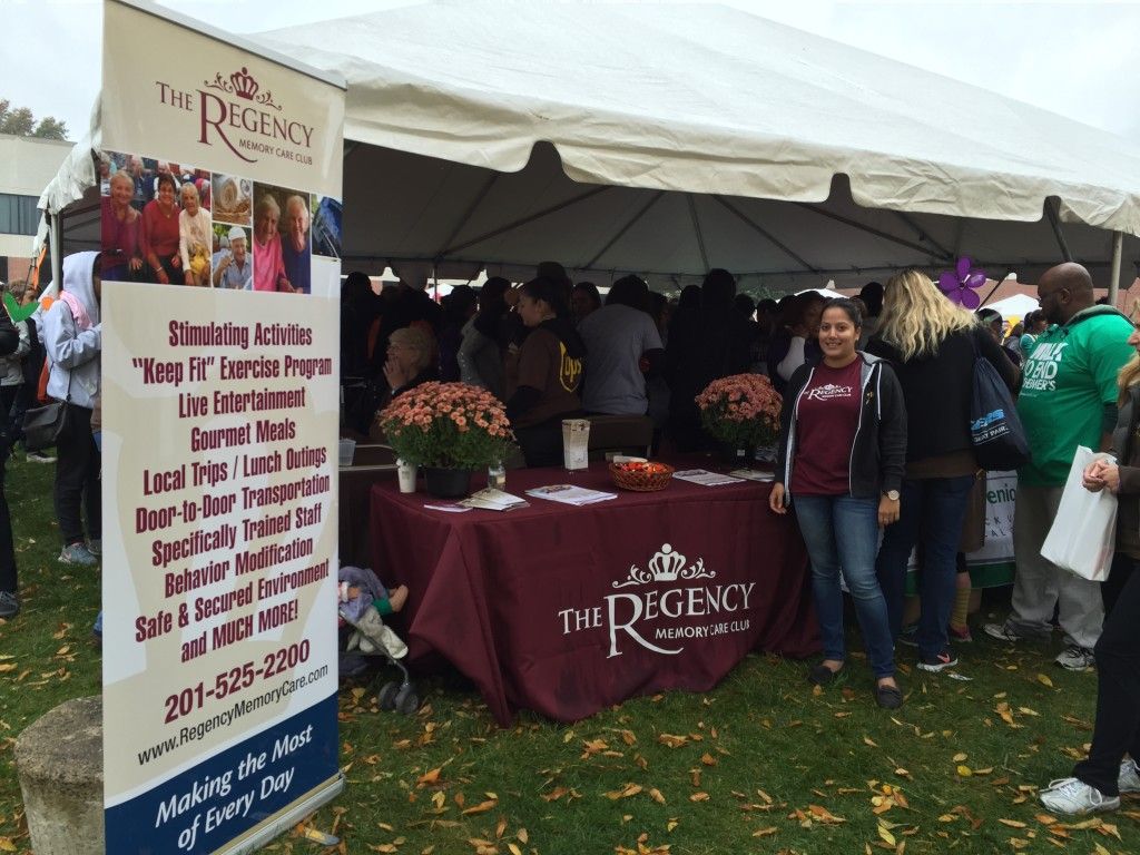 A promotional banner and booth for The Regency, an adult day care center, at an outdoor event under a white canopy.
