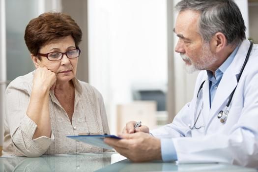 A person listens intently while a healthcare provider explains information on a clipboard in a clinic setting.