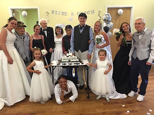 A group poses for a photo at a wedding celebration, with some people in formal attire and two children in white dresses.