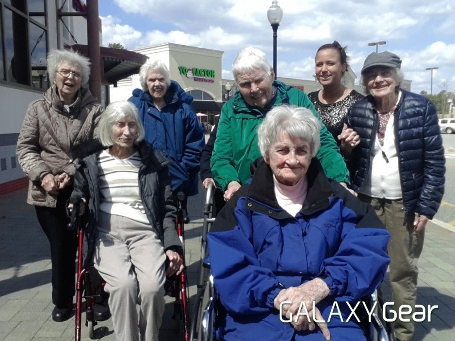 A group of individuals stands and sits in wheelchairs outside a building on a sunny day.