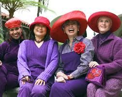 Four people in purple outfits and red hats pose and smile outdoors.