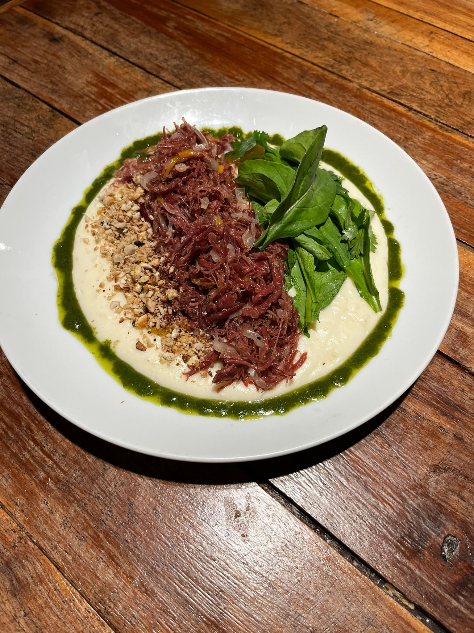 Prato de arroz coberto com carne desfiada, acompanhado de legumes verdes e molho, servido sobre uma mesa de madeira.