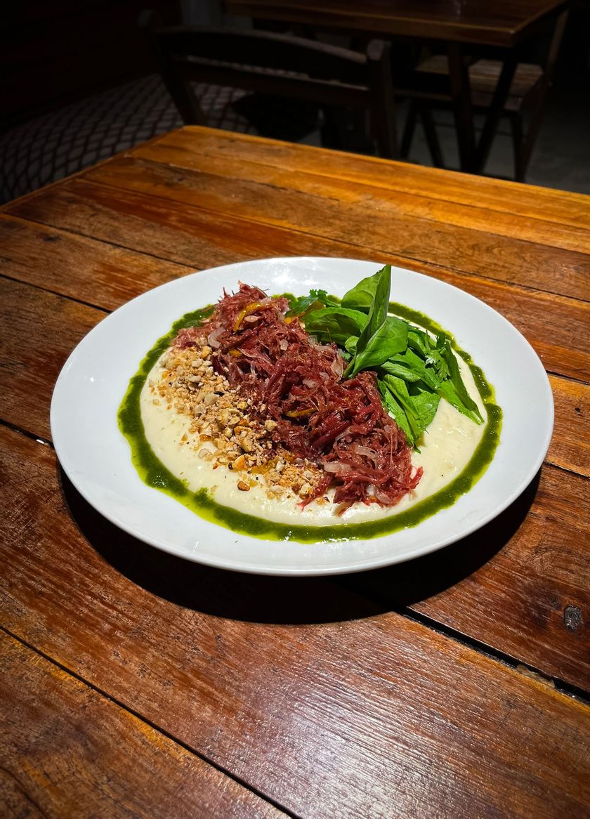 Prato de arroz com molho vermelho e legumes verdes sobre uma mesa de madeira de restaurante.