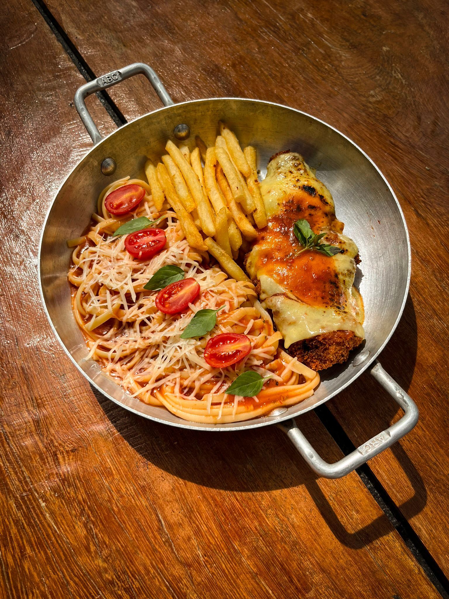 Panela de massa, batatas fritas e peixe assado sobre uma mesa de madeira