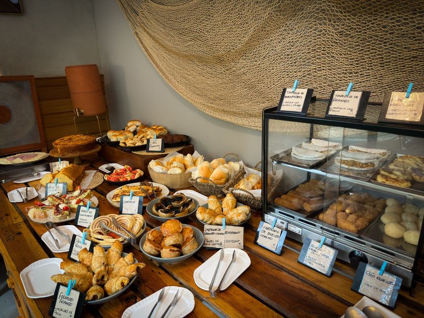 Vitrine de padaria com uma variedade de doces e pães em bandejas e vitrines de vidro em ambiente interno.